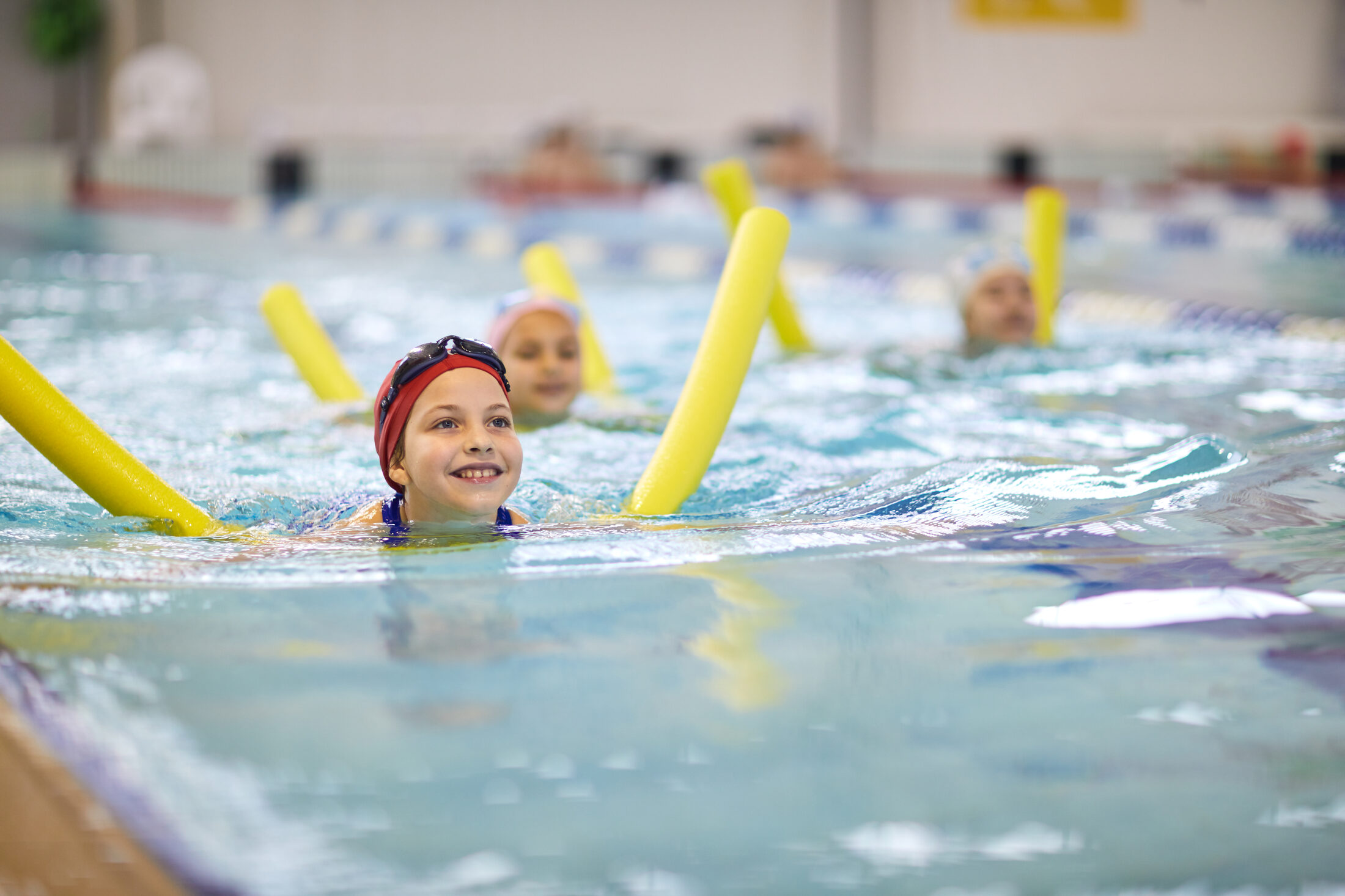Mädchen mit Schwimmnudel im Kinderschwimmkurs